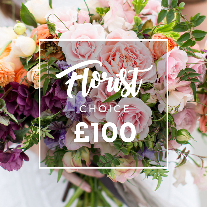 This image shows a hand-tied bouquet arranged with a florist's confident hand: large, soft pink garden roses dominate the centre, their multi-layered petals creating a sensuous, velvety core. Intermingled are peach and coral ranunculus or similar layered blossoms whose tight spirals contrast the open roses, and creamy white tiny flowers that act like soft punctuation points across the bouquet. Deep plum or burgundy hellebores add shaded texture and weight, while pale purple-and-white striped sweet peas drift through the stems offering delicate scent and a sense of movement. A generous mix of greenery - from thin, trailing vines to broader, matte leaves - frames and separates the blooms, producing a loose, garden-inspired profile that feels both refined and spontaneous. A person's hands cradle the bottom of the stems, visible against a faintly blurred light sleeve, suggesting immediate holding and delivery. Over the flowers, a white rectangular overlay reads Florist Choice in an elegant script, with CHOICE in smaller uppercase beneath and a bold ?100 at the bottom, all enclosed by a thin white square outline that makes the offer unmistakable. The bouquet conveys a romantic, bespoke sensibility - ideal for weddings, anniversaries or thoughtful gestures - and reflects the seasonal selections a Mill Hill florist might prepare for delivery to local addresses near Mill Hill Park and Bittacy Hill. This is an expertly curated, tactile arrangement that invites both touch and lingering scent, prepared with the care you expect from Flowers Mill Hill.