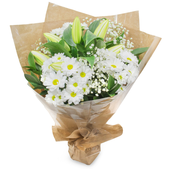 The image presents a fresh, upright bouquet where white and green are orchestrated into a calm, elegant statement. Central to the arrangement are numerous pure white chrysanthemum heads, each with many fine petals surrounding a warm yellow eye that brings a sunny subtlety to the otherwise cool palette. Scattered through these are several elongated lily buds tinged pale green-yellow-some with faint striping-remaining closed and offering the sense of unfolding that makes the bouquet feel alive over time. Sprays of baby's breath (Gypsophila) are threaded between the larger flowers; their tiny, cloud-like blossoms provide a whisper-soft texture and gentle negative space that accentuates the fuller blooms. Rich, dark green foliage gives the composition depth and visual weight, its glossy leaves contrasting with the matte crinkle of the brown kraft paper that wraps the stems from within. Over that sits a clear, glossy cellophane layer that protects the blooms and allows their form and colour to read clearly; the wrapping is gathered and secured at the base so the bouquet may be carried or placed upright. Under soft, neutral lighting the arrangement suggests a clean, delicate scent-fresh stems and a faint meadow-like note-and projects feelings of purity, calm, and thoughtful care. Locally, this kind of bouquet is well suited to the quieter, reflective moments around Mill Hill Broadway or the lanes near Mill Hill East: a considerate choice for get-well wishes, sympathy, or understated celebrations where restraint and grace are desired.