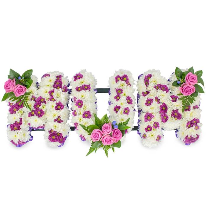 Presented against a pristine white backdrop, this bespoke floral memorial spells MUM in three voluminous, sculpted letters formed from a dense mattress of pure white chrysanthemum blooms that give the piece a pillowy, tactile quality. Scattered throughout the white bed are clusters of vibrant purple and magenta spray chrysanthemum accents that create gentle shading and visual movement across each letter. The composition is softened and defined along its edges by a narrow purple ribbon that subtly outlines the letterforms, while thin dark horizontal bars link the trio of letters and provide the quiet engineering that keeps the tribute upright and unified. Three charming bouquets of vivid pink spray roses are placed with intentional balance: a compact pair crowns the upper left of the first M, a larger cluster of four to five roses nestles within the lower curve of the U, and a mirroring cluster adorns the upper right of the final M. Fern fronds and mixed deep green foliage fan beneath and around the roses, their texture contrasting with the chrysanthemum's fluff, and tiny cerulean-blue accent flowers peek through like soft stars. The lighting in the photo reveals the tactile contours of each petal and the careful layering the florist employed, evoking a hush of remembrance and the quiet dignity suitable for a church memorial or funeral chapel near The Ridgeway or Bittacy Hill. This personalised tribute honours a mother with tenderness, craftsmanship and respectful composition suited to bereavement services in the local Mill Hill area.
