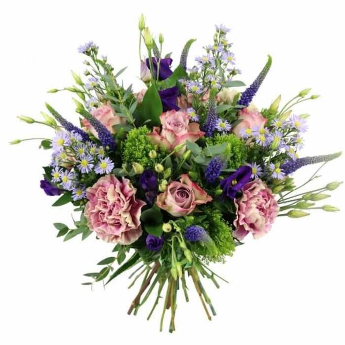 Captured from a slightly elevated angle, this hand-tied bouquet appears full and abundant, its rounded form clearly defined against a pure white background that highlights the nuanced pink and purple tones. At its heart lie several carefully chosen roses in gentle shades of pastel pink, some with petals just beginning to relax from tight buds, others fully open so that their spiralled centres and delicate veining are clearly visible. The outer petals subtly fade toward a softer cream or blush, giving each rose depth and dimension. Interwoven among them are large carnations in dusty rose and mauve, their many ruffled petals forming soft, plush mounds that add a sense of volume and comfort. Emerging from this romantic base, slender stems of Veronica in deep violet and indigo fan upward, their elongated spires introducing vertical structure and a striking contrast, like tall hedgerows glimpsed along Mill Hill's residential lanes. Scattered between these vertical accents are clusters of lisianthus blossoms, their bell-shaped, velvety petals in rich purple shades that deepen the overall palette and guide the eye inward. Throughout the bouquet, small, aster-style flowers in pale lavender-blue with subtle yellow centres create a light, airy weave, giving the arrangement a touch of meadow-like softness. The blooms are supported by a rich mix of foliage: vivid lime-green filler, possibly sedum or green trick dianthus, pops brightly against the petals, while silvery eucalyptus leaves and soft sage greenery curl around the edges, their cooler tones lending balance and calm. The stems are drawn together tightly at the base, trimmed to an even length and left clearly visible, confirming the bouquet's hand-tied craftsmanship, perfect for slipping into a glass vase in a Mill Hill living room. Overall, the design exudes sophistication, warmth, and a sense of celebration, making it a fitting choice for luxury flower delivery, milestone events, or simple yet heartfelt gestures.