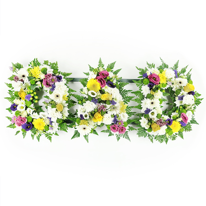 In this image, a floral tribute spelling out DAD sits against a clean, white background, giving the arrangement a timeless, almost gallery-like quality. The three capital letters - D, A, and D - are evenly spaced in a neat row, each one standing solid and self-contained while clearly belonging to the same design. Their edges are framed with a generous collar of rich, deep green fern, the foliage overlapping in soft arcs that both define the letter shapes and add a sense of living, organic movement. Within this verdant outline, every letter is filled edge to edge with fresh flowers, arranged front-facing and tightly massed. The primary impression is one of white: large chrysanthemum blooms and crisp white gerbera daisies create a cushion of softness, each petal layered and slightly curved, catching subtle shifts of light. Threaded through this calm foundation are bright yellow accents - cheerful gerbera daisies and dainty yellow spray roses - introducing warmth, optimism, and the feeling of remembered laughter. To provide depth and contrast, clusters of elegant purple lisianthus and rich magenta or deep pink spray roses are carefully dotted throughout the letters, their saturated hues conveying love, dignity, and thankfulness. Small, bright green button chrysanthemums and fine sprigs of lavender-tinted filler flowers are tucked into any remaining spaces, lending a delicate, detailed finish that rewards closer inspection. Discreet dark bars connect the letters at the base, holding them in a straight line without detracting from the floral work. The overall effect is of a heartfelt, traditional sympathy tribute, the kind a Mill Hill family might have arranged for a father's funeral or memorial, perhaps delivered to a church off Mill Hill Broadway or a quiet chapel up on the hill, where these flowers can speak of affection and remembrance when words are hard to find.