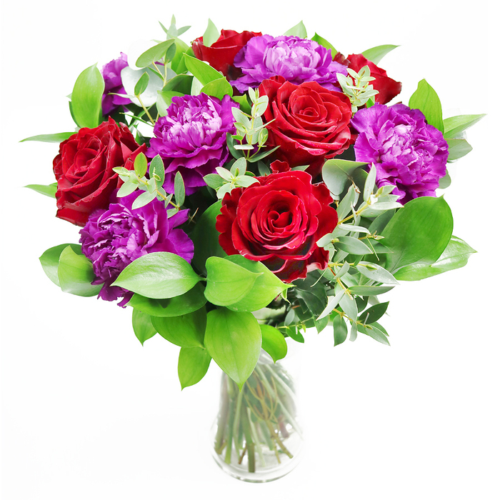 In this bouquet, the timeless appeal of red roses meets the plush elegance of purple peonies, resulting in a composition that feels both classic and contemporary. The roses rise proudly, each bloom at perfect openness, with layers of velvety petals spiralling outward from a deep centre and creating a sense of depth and intensity. Interspersed among them, the purple peonies open in fuller, rounder forms, their numerous, finely ruffled petals producing a texture that softens the sharper outlines of the roses. This interplay of shape and texture is anchored by a foundation of generous greenery: glossy green leaves that extend beyond the flowers add fullness and definition, while lacy strands of eucalyptus weave between blooms, their softly muted, silver-green tones enhancing the cooler notes in the peonies. The arrangement rests in a clear glass vase, where the stems stand in clean water, neatly cut and slightly angled, forming an orderly pattern beneath the exuberant flowers above. Light seems to spill across the bouquet, catching the curves of petals and leaves, and casting gentle reflections on the surface of the vase, as if the arrangement were placed near a window in a Mill Hill home overlooking The Ridgeway or one of the area's leafy gardens. The imagined aroma is delicate yet layered: the gentle sweetness of rose lifted by the invigorating, almost spa-like scent of eucalyptus, evoking the fresh, open-air feeling of a morning walk through Mill Hill Park. This bouquet would suit an anniversary table, a significant birthday, or a warm gesture sent to family or friends around Mill Hill Broadway, expressing admiration and affection with calm, confident beauty.