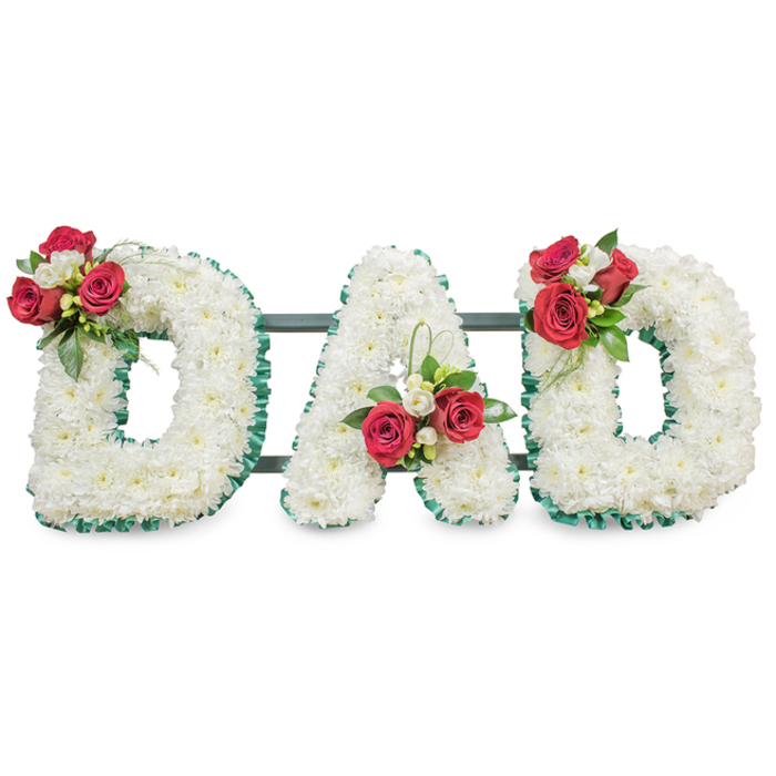 A solemn, carefully composed floral tribute that spells the word DAD in bold block capitals, each letter densely covered with pristine white chrysanthemums to create a smooth, soft-textured surface that reads as both pure and reverent. The letters are crisply outlined with a pleated emerald-green ribbon, which highlights their shape and adds a stately contrast to the white mass of blooms. Thoughtfully positioned floral clusters punctuate each letter: the left 'D' carries a prominent spray of deep red roses paired with fragrant white freesia and glossy greenery on its upper curve; the central 'A' bears a similar grouping near the lower left diagonal, with a pale loop of foliage drawing the eye upward; and the right 'D' mirrors the first, completing a carefully balanced composition. Thin, dark-green or black horizontal support bars are visible behind the letters, providing discreet stability and ensuring the display stands as a unified tribute. Under soft, even lighting the chrysanthemums read as ivory-white, the roses as velvety crimson, and the freesia as delicate white accents - together they form a message of devoted love and respectful remembrance. For families in Mill Hill Village, Mill Hill Broadway and surrounding streets arranging a funeral or memorial, this is a traditional yet personal choice. Flowers Mill Hill can produce similar bespoke letter tributes for local services, crafted with the care and sensitivity such farewells deserve.
