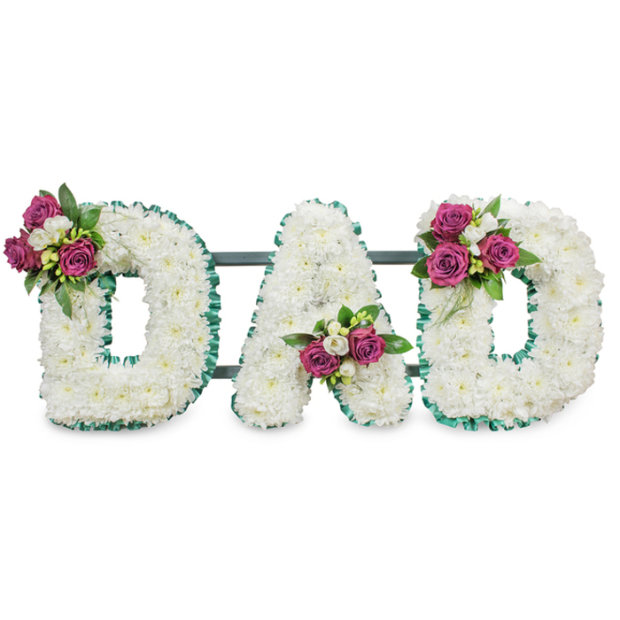 A striking memorial arrangement spells the word DAD in three bold, sculpted letters, each letter formed from a dense layer of pristine white chrysanthemums that give the piece a soft, cloud-like texture. The white surface is crisply edged with a ruffled emerald-green ribbon, which traces both the outer and inner contours of each letter and supplies a clear, respectful frame against the white backdrop. Behind the letters a muted dark green or grey horizontal support is visible, hinting at the sturdy easel or stand that would present this tribute at a service. Carefully placed accent bouquets punctuate the composition: clusters of deep fuchsia or magenta roses in varying opening stages are nestled with small white freesias or similar delicate spray flowers and complemented by rich dark-green foliage to add depth and contrast. The first D bears its bouquet on the upper left curve, the A holds its cluster low in the central V, and the final D mirrors the first with a cluster on its upper right curve, producing a deliberate, comforting balance. The overall mood is one of solemn affection-a classic, personalised sympathy piece chosen to honour a beloved father at a funeral, memorial service, or graveside. Locally, such lettering tributes are often requested by Mill Hill families when arranging services near Mill Hill East or the Parish churches, and the design reads both traditional and intimate, a visual expression of love and remembrance crafted with florist's care.