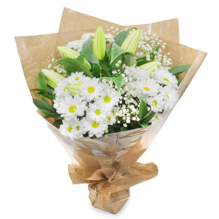 This hand-tied bouquet of white and green flowers is photographed against a pristine white background, allowing every nuance of texture and tone to stand out with clarity, as if the arrangement had just been placed down in a bright Mill Hill shop. The design is dominated by clusters of white daisy-like chrysanthemums, perhaps one of the long-lasting varieties favoured by florists in the area. Each flower shows multiple layers of slender petals, pristine and unmarked, circling a distinctive yellow-green centre that adds quiet warmth and focus to the display. Among these blooms, tall lily buds emerge, their petals still closed and tinted a soft, cool green that gradually fades to creamy white at the tips. The buds point gently upwards, their smooth forms suggesting the slow, dignified opening of future fragrant blossoms over the coming days. Fine branches of white baby's breath wind between the larger flowers, offering a delicate, airy presence that lightens the overall silhouette and recalls the soft haze of early morning over Mill Hill's open spaces. Encircling the flowers is a generous layer of deep green foliage, glossy and fresh, providing contrast, shadow, and a sense of natural abundance. The stems are wrapped in brown kraft paper that has been folded and crinkled with intent, forming a rustic yet elegant cone that feels authentic and hand-crafted. A transparent cellophane layer sits over the paper, catching hints of reflection while still revealing the stems, leaves, and careful binding beneath. The base of the bouquet is neatly gathered and tied, giving a tidy, ready-to-present finish. This arrangement communicates purity, sincerity, and calm, making it a fitting choice for sympathetic occasions, quiet farewells, or thoughtful messages of support to friends and family in Mill Hill and neighbouring areas.