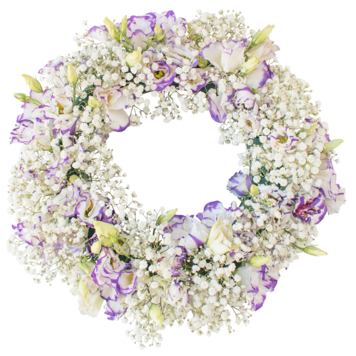A beautifully structured funeral wreath lies against a completely white background, its subtle colours and textures brought into clear focus by the simplicity of the setting. The wreath forms an immaculate circle, thick with sprigs of Baby's Breath that create a soft, misty base. These tiny, cloud-like white blossoms cover every part of the ring, giving the arrangement a sense of airiness despite its fullness. Rising above this delicate foundation are clusters of lisianthus, their petals arranged in gentle ruffles that catch and hold the light. The lisianthus blooms are predominantly white, yet every petal edge is traced with purple, ranging from the palest lavender wash to deeper violet accents. This careful edging lends each flower a hand-painted quality, as though the colour has been softly brushed into place. A number of buds are tucked between the open blooms, slim green stems tipped with creamy, closed petals that carry just a hint of the purple to come, suggesting ongoing life and memory. The florist has placed the lisianthus evenly around the wreath, ensuring the purple touches create a harmonious rhythm rather than strong blocks of colour. The inner circle of the wreath remains wide and open, a quiet void at the centre that naturally symbolises the space left by a loved one's passing. The design feels well suited to services in the Mill Hill area, perhaps set on a stand near the altar or laid as a graveside tribute after a ceremony close to Mill Hill Broadway. Created with the practiced hands of Flowers Mill Hill, the wreath radiates calm, respect, and the gentle beauty of a carefully considered goodbye.
