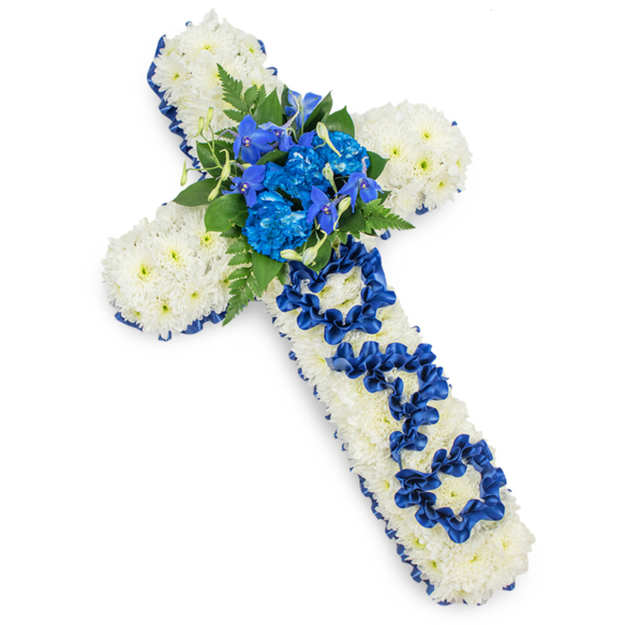 A large funeral cross, meticulously arranged in white and royal blue, is displayed against a seamless white background that makes every detail stand out. The entire cross is cloaked in tight clusters of white spray chrysanthemums, their petite blooms forming a thick, cushion-like surface. Each chrysanthemum head is gently domed, with layered petals that lend a soft, almost feathery appearance. This uninterrupted field of white sets a tranquil, reverent tone, much like the quiet corners of Mill Hill's green spaces where families gather to reflect. Outlining the cross, a deep royal blue satin ribbon has been carefully attached along all sides. The ribbon follows every curve and corner, creating a crisp, defined edge that adds structure and a touch of formal elegance to the design.   

At the heart of the cross, a central spray of blue flowers rises from the white chrysanthemum base. Full, frilly blue carnations, likely dyed to match the rich royal shade, are grouped together with slender, upward-pointing flower spikes that resemble blue delphiniums or orchids. This combination introduces depth and variety, drawing the eye into the centre. Surrounding the blue blooms, dark green fern fronds and smooth, glossy leaves extend outward in soft arcs, adding texture and a sense of natural movement. Down the middle of the vertical arm, the word DAD is created using the same royal blue satin ribbon as the border. Each letter is skillfully looped and arranged, clearly legible against the white background and visibly crafted by hand. This personal inscription gives the tribute a poignant, intimate quality, ideal for honouring a father at a funeral service, memorial gathering, or graveside ceremony in Mill Hill. The overall effect is one of composed grace, expressing love, respect, and a lasting farewell.