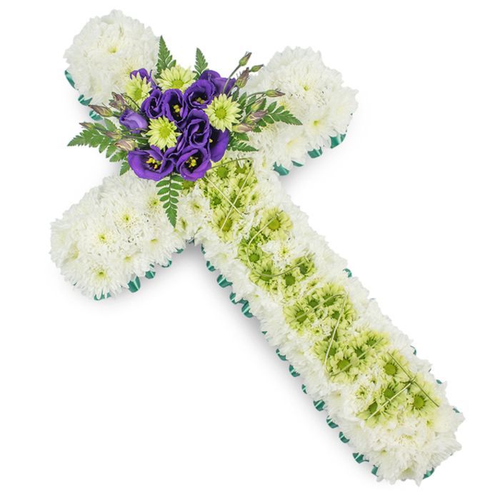 A thoughtfully crafted floral cross, perfectly suited to a Christian funeral or memorial in Mill Hill, is shown in clear detail against a smooth white background. The cross's structure is entirely cloaked in a lush carpet of white spray chrysanthemums, each bloom carefully placed to form a seamless, cloud-like surface that runs from the topmost arm down to the base of the design. This solid field of white, uninterrupted and pure, conveys peace, reverence, and a sense of quiet prayer. Framing the shape, a border of bright green ribbon or meticulously folded foliage follows every curve and angle, giving the cross a defined silhouette and a fresh contrast that recalls the open spaces around Mill Hill and Arrandene. Along the centre of the vertical stem, a rectangular inlay of lime green button chrysanthemums adds a delicate yet distinct accent, standing out gently against the soft white background of petals. Across this green panel, extremely fine pale green wires or strands are draped in a loose, diamond-like lattice, introducing a layer of fine detail that speaks of the florist's steady hands and design precision. At the very centre, where the arms intersect, lies the focal spray: rich purple lisianthus (eustoma) blooms, with their elegantly ruffled, velvet-textured petals, are clustered alongside lime green chrysanthemums, echoing the stripe below. This central grouping is surrounded and softened by dark green fern fronds and tapered leaves that extend slightly beyond the cross's surface, adding depth and a touch of natural movement. The result is a dignified, symbolic tribute, well suited for church services or graveside ceremonies in Mill Hill, offering a gentle yet expressive way to honour and remember a loved one.