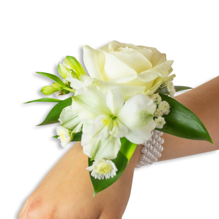 Set against a pristine white background, this wrist corsage is presented from a slightly elevated angle, the wearer's fair skin lending a gentle contrast that highlights the arrangement's purity. Central to the piece is a creamy ivory rose whose petals unfurl with velvety grace, creating a calm focal point. Below and a touch left of centre, a prominent white trumpet-shaped bloom-suggestive of alstroemeria or a small lily-exposes a pale green-yellow centre that adds subtle depth and botanical interest. Interlaced among the primary flowers are delicate sprays of baby's-breath-like filler, their minute white blossoms forming a soft, clouded texture that cushions and lifts the main blooms. Several small, green-tinged buds suggest imminent opening, introducing a narrative of growth, while a cluster of tiny daisy-like white flowers with sunny yellow centres brings a gentle, approachable charm. Lush, smooth deep-green leaves frame the composition, their glossy surfaces punctuating the whites and reinforcing the corsage's organic fullness. The fastening is an elegant, elastic multi-strand pearl bracelet: strings of near-identical round pearls encircle the wrist, providing both secure wear and a refined vintage note. The overall mood is poised and celebratory-an ideal accessory for weddings, formal dances, or civil ceremonies-and reflects the kind of considered, handcrafted work we create for clients around Mill Hill Broadway and neighbouring streets, where floral pieces are made to feel both timeless and intimately local.