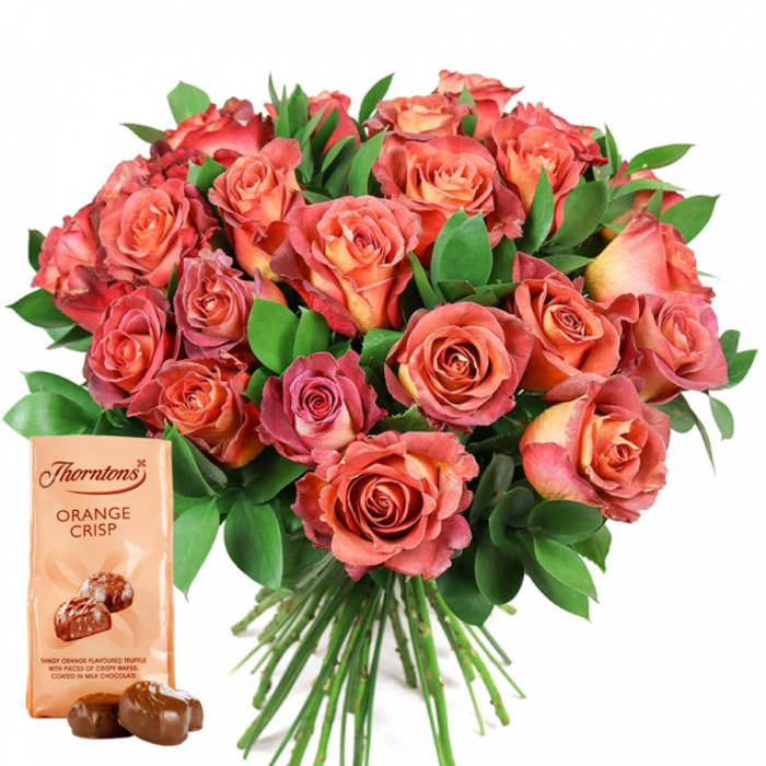 Dominating the image is a lush bouquet of roses, their rounded heads gathering like a cascade of Mill Hill Manor's blooms after spring rain. The roses showcase a dazzling interplay of colour, moving from softly glowing peach and pale cream hearts to assertive coral and deep-pink outer petals in an effortless ombre effect. Velvety, tightly layered petals hint at exceptional freshness, a hallmark of local floristry prowess. Intertwined among the blossoms, dense dark green leaves-possibly ruscus or eucalyptus-provide a lively, verdant accent, their glossy surfaces catching light in a way that frames the flowers with natural elegance. Just below, angled in the lower left, a classic Thorntons Orange Crisp chocolate pouch stands out: the smooth, pale packaging highlighted by the iconic brand logo and a truffle illustration beneath the words Tangy orange flavoured truffle with pieces of crispy wafer, coated in milk chocolate. In front, two unwrapped orange crisp truffles maintain their glossy finish, reflecting the promise of sweet delight within. The composition, set on pristine white, tells a story of celebration and thoughtful gifting-perfect for birthdays, anniversaries, or spontaneous gestures of love and gratitude in Mill Hill. Every detail, from the brilliant florals to the handcrafted sweets, reveals the expertise and warmth that goes into every offering from Flowers Mill Hill.