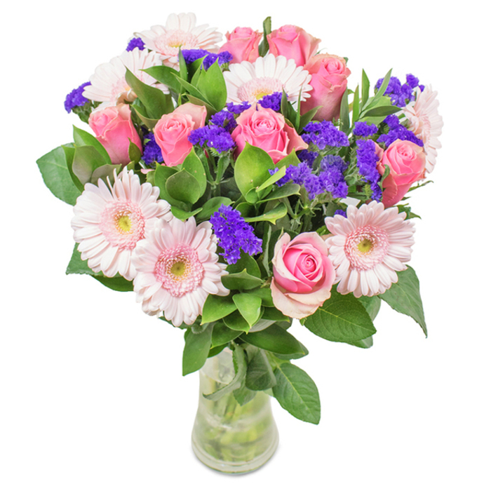 This striking bouquet, freshly arranged in Mill Hill and set against a pristine background, showcases a careful balance of refinement and vibrancy, reminiscent of the area's leafy avenues and warm community gatherings. The centerpiece features approximately eight pink roses-some with tightly furled buds, others just unfurling their classic spirals-blending blush to richer rose tones. Framing the roses are about seven pale pink Gerbera daisies, easily recognized by their broad, cheerful faces and near-white centers, injecting the design with softness and airy light. Scattered between, clusters of intense purple filler flowers-likely statice or limonium-add bold texture and pockets of depth, just as bursts of color enliven the local shops and parks. The foundation is a lush base of deep green foliage, its abundant greenery reminiscent of nature walks around Arrandene Open Space. The transparent vase, filled with clear water and tidy stems, furthers the sense of freshness and care typical of Flowers Mill Hill's deliveries. This versatile bouquet is ideal for occasions from birthdays to Mother's Day, or as a welcoming accent for a Mill Hill home or office, expressing happiness, warmth, and genuine affection through its radiant, thoughtfully composed blooms.