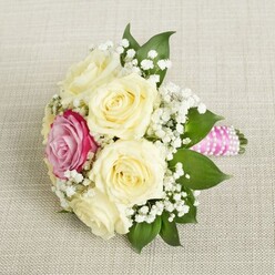 Imagine the gentle hush of a Mill Hill morning, echoed in this sophisticated bouquet poised on a creamy, subtly woven textile akin to those in the area's charming homes. The arrangement is anchored by creamy ivory roses, each in full bloom, their velvety petals spiraling outward in an embrace of romance and celebration. A single magenta-pink rose glows with vibrance, positioned just off-center and lending a unique charm reminiscent of the bold camellias found in Mill Hill's elegant gardens. White baby's breath floats between the blooms, imparting an airy, delicate halo, while glossy green leaves provide a rich and grounding flourish. The stems are bound together in bright pink satin ribbon, with a spiraling accent of lustrous white pearls-adding a contemporary yet timeless elegance. Natural light bathes the bouquet, accentuating its textural contrasts and the delicate interplay of colors. Whether chosen for a wedding by the bustling Broadway or a special event near Arrandene Open Space, this bouquet embodies the care and artistry that define Flowers Mill Hill.