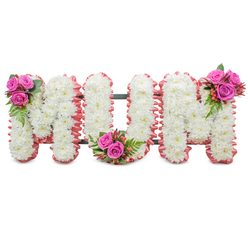 A profoundly respectful funeral tribute, this standing arrangement spells "MUM" in three bold capital letters, each letter formed from an abundant mass of pure white chrysanthemums. The tiny, dense blooms create a velvety, uniform texture that reads as immaculate and consoling; their cool white petals suggest purity and remembrance. A delicate, ruffled blush-pink ribbon trims each letter's perimeter, the soft fabric edge introducing a gentle warmth and a subtle, tactile contrast against the crisp chrysanthemum faces. Visible between the letters is a dark green support frame that gives the whole tribute its shape and steadiness without distracting from the floral surface. Three compact clusters of accent flowers are placed with considered balance: a spray of deep fuchsia roses, glossy greenery and orange-red hypericum berries nests at the top left of the first M, a matching cluster sits in the base curve of the U, and the final M is finished with a similar bouquet on its upper right. The roses' velvety perfume and the chrysanthemums' lighter, green-tinged scent mingle into a quiet, comforting aroma. As a Mill Hill florist I picture this arrangement standing at a family memorial near Mill Hill Broadway or laid beside a service at the local church, a piece that speaks of love and steady care. At Flowers Mill Hill we often use this combination of classic whites with pink accents to convey respect, warmth and lasting affection when families gather to say goodbye.