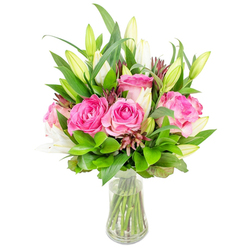 Imagine a freshly composed arrangement that reads like a small, joyous garden captured in glass: deep pink roses with satin-like petals cluster at the centre, their colour moving from intense fuchsia at the heart to softer blush tones at the petal edges. Intertwined among them are pristine white lily buds-some buttoned and green-tipped, others beginning to open into delicate trumpets-providing a sculptural contrast in both shape and tone. Lush green foliage surrounds and supports each bloom, from larger pointed leaves that give structure to finer, glossy sprigs that catch light and offer a soft, textural backdrop. Scattered throughout are tiny darker burgundy accents and seed-like buds that give the bouquet a lived-in, natural feel and add quiet complexity to the overall palette.

The stems sit in a clear, slightly tapered glass vase filled with clean water; you can see the fresh green stems through the glass, which reinforces the sense of crisp freshness. As a Mill Hill florist I compose arrangements like this to evoke celebration without fuss: it reads equally well in a bright kitchen or as a refined gift. Flowers Mill Hill prepares and packs pieces like this with care for local drop-offs around Mill Hill Broadway, The Hale and nearby roads, aiming to keep that just-cut scent and vibrant colour intact. The overall impression is one of thoughtful elegance-a bouquet that says congratulations, thank you, or simply 'I'm thinking of you' with quietly confident charm.