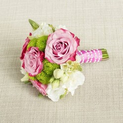 Resting lengthways on a pale, textured fabric that resembles a finely woven linen tablecloth, this compact bouquet feels like a quiet moment of celebration captured in flowers. The eye is first drawn to three lush pink roses, their blooms fully open yet still holding a gentle curve at the centre. Each petal carries a delicate gradient of colour, starting as soft pastel rose at the heart and deepening into rich pink, almost magenta, around the ruffled edges, giving the roses a velvety depth. Tucked between these are vivid lime-green button chrysanthemums, their round, cushion-like heads formed of countless tiny florets that create a fresh, almost playful texture against the classic roses. Surrounding and softening the composition, clusters of white and cream filler flowers-suggestive of lisianthus, freesia, or dainty waxflower-bring a cloud-like lightness, with a few miniature star-shaped blossoms and sunny yellow centres adding a touch of brightness. On the right, the stems are neatly hand-tied and bound in a smooth band of bright fuchsia satin ribbon, which catches the light with a gentle sheen. Over the ribbon, a slim strand of white faux pearls is wound diagonally, crossing back and forth like an elegant piece of jewellery, while the trimmed green stems peek out at the base, clean and fresh. The lighting is soft and even, with no harsh shadows, creating a calm, intimate atmosphere. It feels like a bridesmaid's bouquet paused on a table before a ceremony in Mill Hill, perhaps on the way from a home near Mill Hill Park to a reception nearby, blending tradition with a modern burst of colour.