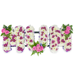 Carefully assembled and photographed on a plain white background, this three-dimensional floral tribute spells out MUM in bold capital letters made from a dense base of snowy white chrysanthemums that create a plush, tactile surface. Throughout that white foundation, small pockets of deep purple and magenta pom-pom style blooms are artfully placed to introduce shadow and rhythm, while a trio of bright pink spray roses form the tribute's focal bouquets: a small cluster at the upper left of the first M, a larger, more generous grouping nestled into the lower curve of the U, and a matching cluster at the upper right of the final M. Lush fern fronds and varied dark green foliage cradle each rose cluster, their serrated edges and glossy leaves providing contrast to the soft chrysanthemum petals; fine blue accent blooms are sprinkled among the greenery like quiet notes. A slim, dark linking bar runs horizontally to connect the letters, lending structural cohesion to the piece without distracting from the overall tenderness. The arrangement reads as both an expression of deep love and a calming visual for funeral spaces-softly lit petals, gentle colour transitions and a subtle scent of fresh chrysanthemums that suggests comfort. Crafted with care by local hands, this style of personalised tribute is one we often prepare for families across Mill Hill Village and Mill Hill Broadway, and Flowers Mill Hill can reproduce the design to suit service spaces or a memorial display with sensitivity and attention to detail.