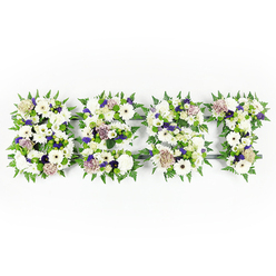 This serene floral tribute spells DAD across a horizontal tapestry of whites, lilacs, and fresh green foliage, crafted to offer calm and comfort in a moment of grief. Each letter is built from a plush mix of velvety chrysanthemums, ivory gerbera daisies with their clean silhouettes, and soft, pastel coffee-hued roses that bring a gentle, warm tone to the predominantly white palette. Interspersed among them are ruffled white carnations and slender lisianthus, their layered petals catching the light and adding a tender, tactile quality. Small sprays of violet statice and deeper mauve filler flowers provide subtle pockets of colour that lift the composition without overwhelming it, while compact green button chrysanthemums sit low and bright, adding texture and fresh contrast. The edges of each letter are carefully lined with vibrant fern fronds, their crisp, feathered shapes creating a natural border and a sense of graceful movement that frames the name with dignity. A dark structural base underpins the arrangement and is discreetly visible in places, lending shape and strength to the finished piece. Imagine the soft, comforting scent of roses and carnations mingling with the cool green fragrance of fern - an olfactory memory that lingers alongside the visual. This arrangement feels especially suited to local services and family gatherings in Mill Hill, from intimate wakes to church memorials, where a personal tribute to a cherished father speaks more clearly than words. As a florist working around Mill Hill Broadway and the Village, I arrange these with the quiet attention and care the moment calls for, mindful of the small details that make a farewell feel lovingly composed.