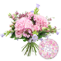 This image presents a romantic birthday bouquet and balloon pairing, set against a clean, white backdrop that resembles the calm, bright interiors of homes near Mill Hill Park. Dominating the arrangement, generous clusters of blush pink hydrangea create a soft, cloud-like mass, their tightly packed petals forming rounded heads that seem to billow outward. Between these luxurious hydrangeas, soft pink roses appear at different moments in their blooming cycle: fully opened flowers show off their layered, swirling centres, while firm buds stand nearby, waiting to unfurl in the days after delivery. Dotted through the bouquet, tiny fuchsia-pink blooms - likely waxflower or a similar filler - lend texture and a splash of deeper colour, giving the design a relaxed, garden-picked charm that would look at home on a table overlooking Mill Hill's leafy streets. Slender spikes of campanula rise delicately among the larger blooms, their bell-shaped flowers opening in shades of lavender and periwinkle, adding vertical interest and a refreshing coolness to the warm pink palette. Surrounding all of this, fresh green foliage flows outward in different shapes and sizes, from long, tapering leaves to more substantial greenery that frames and supports the composition, enhancing its sense of fullness and natural movement. The stems below are clearly gathered and aligned, a hallmark of a carefully crafted hand-tied bouquet. To the lower right, a round foil birthday balloon brings in a playful, festive element. Its metallic surface is printed with a fine pattern of small roses and buds in coordinating pink, cream, and lavender tones, while the centre carries the words "Happy Birthday" in elegant purple script. Together, the flowers and balloon form a complete birthday gift set, perfect for surprising someone in Mill Hill with a blend of beauty, colour, and celebratory spirit.