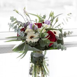 Amidst the gentle sunlight typical of a Mill Hill morning, this luxurious bouquet emanates an understated elegance. The sumptuous red roses at its centre speak of deep affections, their petals folding in layers of velvet richness. White gerberas, with their sculptural petals and dark brown eyes, add an airy lightness that brightens the entire composition. Soft purple lisianthus, some still in the bud, provide a dreamy pastel allure, casting a sense of hope and unfolding potential. Generous eucalyptus sprigs, silver-green and aromatic, arc elegantly outwards, echoing the gentle hills around Mill Hill Broadway. Voluminous white filler flowers drift between the main blooms, imparting a gentle, cloud-like fullness. Wrapped in lush structural greenery at the base, the bouquet sits confidently in a sparkling glass vase, each stem crisply visible in the clear water below. Whether chosen as a thoughtful gift for an anniversary or to add serenity to a home on Hale Lane, this arrangement reflects both the refined artistry and heartfelt care that define Mill Hill's local floristry scene.
