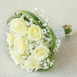 Imbued with a sense of gentle sophistication, this masterfully curated bouquet rests on a lightly textured, neutral fabric-a nod to the elegant simplicity appreciated in Mill Hill's close-knit neighbourhoods. The focal point is a gathering of creamy white and pale butter-toned roses, their petals unfolding in soft spirals that whisper of love's quiet promise. Billowing clusters of delicate white baby's breath nestle between the roses, lending a light, lace-like texture that brings to mind the gentle haze over Arrandene Open Space on a sunny morning. Wide arcs of fresh, slender greenery-possibly artfully looped bear grass-add both movement and structure, encircling and supporting the blooms in harmonious balance. The bouquet's stems are precisely bound, their verdant ends peek from beneath a chic, silvery ribbon handle lavishly embellished with dainty rows of pearl beads-a tactile finishing touch that conjures memories of Mill Hill's storied traditions and festive gatherings. Whether chosen for an intimate wedding at a local venue or as an expression of heartfelt congratulations, this bouquet delivers a message of pure joy and quiet celebration, blooming with local craftsmanship and elegance.