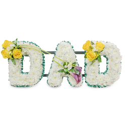 A heartfelt sympathy tribute formed as three large, freestanding block letters spelling 'DAD', each letter densely sheathed in pristine white spray chrysanthemums or similar tiny white blooms to create a soft, textured face. The letters are outlined in a ruffled, dark green satin ribbon that gives a formal, refined edge against the white background, while slim dark-green metal bars are discreetly visible behind them to hold the composition together as one steady unit. The left 'D' is accented on its upper left curve with a glowing cluster of bright yellow roses - roughly three to four open heads - mingled with small white freesias and fresh green foliage; two long, graceful green stems extend diagonally toward the centre, lending a natural line across the trio. The centre 'A' carries a composed spray on its lower left diagonal: two striking deep purple or burgundy calla lilies form a sculptural, reverent heart to the design, surrounded by tiny white accents and verdant leaves. The right 'D' mirrors the left with a matching burst of sunny yellow roses and white filler on its upper right curve. The whole piece sits in soft studio light against a plain white backdrop, emphasizing texture and tone rather than flash; its scent would be a clean, gentle blend of chrysanthemums and roses. As a Mill Hill florist I often prepare similar tributes for services near Mill Hill Broadway, Mill Hill Village and the nearby chapels - Flowers Mill Hill can deliver this bespoke memorial locally with careful handling and dignity.