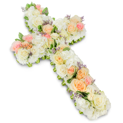 A beautifully arranged floral cross fills the image, a tender funeral tribute that balances classic Christian symbolism with the gentle comfort of pastel flowers. Set against a clean, bright white background, the cross is completely covered in blossoms, forming a thick, velvety surface of petals. Large roses in shades of ivory, cream, soft peach, and blush pink are carefully placed along the length and breadth of the cross, their open blooms revealing delicate, layered centres. They are supported by generous clusters of white hydrangea or similarly fluffy flowers, which lend a plush, cloud-like appearance and create an impression of softness and embrace. Tiny white spray roses and compact filler blooms fill in around the main flowers, adding detail and preventing any gaps, so the cross appears full and expertly finished. Wisps of lavender or pale purple filler flowers are woven in with restraint, contributing discreet touches of colour that enhance the serenity of the overall design. Peeks of green foliage at the edges and beneath some blooms help to subtly frame the cross and bring a hint of outdoor freshness, reminiscent of the calm green spaces around Mill Hill's churches and chapels. The arrangement's soft, rounded edges and carefully balanced proportions give it a sense of calm order and grace. Photographed in bright, even light, every petal and texture can be appreciated, from the velvety rose petals to the feathery filler flowers. This floral cross feels like a deeply respectful choice for a funeral, memorial, or graveside service in Mill Hill, offering visual comfort, spiritual reassurance, and a gentle way to honour a life well lived.