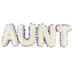 As a florist's keeping, this tribute takes the simple word AUNT and turns it into a quiet, tactile memorial composed entirely of white spray chrysanthemums. Each letter is densely arranged so the small, multi-petalled heads form a continuous, velvety surface; some florets reveal soft yellow centres that lend a gentle warmth to the otherwise pristine white field. A rich purple satin ribbon follows the outline of each letter, its sheen catching the light and folding into tiny pleats that add sculptural depth and a subtle contrasting edge. The letters rest against a spotless white plane, with delicate grey shadows beneath that speak to the work's three-dimensional construction and the sturdy frames that support the blooms. A faint, green-floral scent rises when one leans in, familiar and comforting rather than overpowering.

Crafted with care, this composition aims to honour and console: the chrysanthemums evoke long-lasting remembrance and devotion, the purple ribbon speaks of dignity and thoughtful mourning. The arrangement is presented in a calm, soft light that highlights texture and form, making it fitting for services in local Mill Hill chapels or private remembrances near Mill Hill Park. The overall mood leans toward gentle celebration of memory-steady, tender, and carefully proportioned-offering a personalised way to say goodbye to a cherished family member.