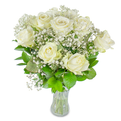 There is an unassuming serenity in this hand-arranged display: a cluster of roughly twelve creamy white roses, each bloom at a slightly different stage of opening, gathered with clouds of delicate baby's breath against a flawless white backdrop. The roses' petals appear plush and thick, their edges curling in a slow, natural rhythm that reads as both resilient and gentle. Between the larger flower faces, fine sprays of gypsophila float like spun sugar, lending the composition a diaphanous, almost musical texture that offsets the roses' density. A verdant bed of greens-from deep, cool emerald to sprightly lime-cradles the blooms, the leaves' matte and glossy surfaces providing subtle contrast and depth. The bouquet is arranged in a clear glass vase that exposes neatly cut stems and a visible water level, a small, honest detail that speaks to freshness and careful handling. Light here is soft and diffused, reminiscent of an early spring morning filtering into a conservatory, and the scent is faintly floral, brightened by green notes rather than heavy perfume. As a florist who knows the rhythm of Mill Hill mornings and the quiet corners around Mill Hill Broadway, I imagine this arrangement bringing a pause of calm to a kitchen table, a small celebration on a mantelpiece, or a gentle sympathy gesture at a local wake. It feels composed, intimate, and reliably comforting-a floral expression of steady affection and thoughtful presence.