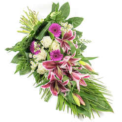 Set against a pure white background, this elegant sympathy spray draws the eye along a diagonal path from the neatly tied stems at the top left to the soft, tapering foliage at the bottom right, creating a natural, flowing teardrop silhouette. The central blooms are striking Stargazer lilies, their generous petals glowing in intense fuchsia-pink and edged in white, scattered with deep burgundy speckles that add depth and character. Some lilies are fully open, revealing their pollen-dusted stamens, while others remain as smooth, elongated buds in soft green and pink. Interspersed with them, vivid magenta gerbera daisies offer bold, daisy-like faces, standing out against the serene backdrop of creamy white roses and ruffled white carnations that lend a sense of peace and purity. Tiny white filler flowers are woven thoughtfully through the larger stems, bringing an airy brightness and a hint of garden-like wildness. The blooms are anchored by a wealth of greenery: broad, glossy dark green leaves provide structure; fine, feathery ferns add a light, textural edge; and long, arching leaves extend and cascade to accentuate the elongated form. The whole arrangement appears freshly made, as though a seasoned florist in Mill Hill has just completed it in a quiet workshop not far from Mill Hill Park, ready for delivery to a nearby church or crematorium. The mood is respectful and tender, well suited for funerals, memorials, or condolence deliveries across Mill Hill, Hendon, and Finchley, offering comfort and a graceful visual tribute to a life remembered.