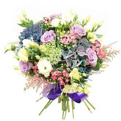 This opulent floral arrangement, assembled by a Mill Hill florist with true passion, bursts with the richness and variety of the neighbourhood's own gardens and commons. Plush hydrangea blooms in indigo, teal, and dusky purple weave together at the bouquet's heart, their soft petals recalling morning mist across Mill Hill's open spaces. Intertwined are roses in gentle lavender and clean white, each blossom unfurling in layers that speak of romance and refined beauty. Billows of white ranunculus introduce plush texture and a delicate, cloud-like feel, harmonizing with the core flowers. Pale yellow lisianthus buds and partially open eustoma blossoms rise between larger blooms, lending lightness and an airy aspect that echoes early spring hedgerows near Bunns Lane. Sprays of vivid fuchsia-pink filler and feathery pale pink astilbe provide playful highlights, filling the bouquet with dynamic energy. Fine, lacy clusters of Ammi Majus introduce intricate detail and soft, cool green accents, enhancing the design's overall depth. Framed by glossy, dark green foliage, this generous bouquet is expertly bound at the base with a luminous royal purple satin ribbon-its sheen a finishing flourish for any special occasion in Mill Hill. Perfect as a gift for milestones, expressions of romance, or uplifting gestures, this bouquet promises to bring a breath of Mill Hill's floral beauty to every doorstep.