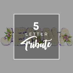 This image showcases a refined five-letter floral tribute, laid out horizontally on a smooth, light grey backdrop that lets the textures and colours stand out with quiet elegance. The letters, likely forming the name "JOHN A," are filled to the edges with immaculate white chrysanthemums, each bloom nestled tightly against the next to create a plush, even surface, much like an expanse of fresh snow over the open spaces of Mill Hill Park. A narrow band of deep purple satin ribbon outlines each character, giving structure and a gentle hint of richness, while subtly guiding the eye along the word. Accents of colour and greenery are carefully placed along the tribute: small arrangements of pale pink and mauve spray roses, some just beginning to unfurl, are grouped with light, feathery fronds of green fern and a few glossy leaves. These clusters sit at a slight angle, suggesting the natural way flowers might rest when laid by hand, and adding a touch of movement to the otherwise orderly display. Over the central section of the letters, a square block of slightly darker grey carries the words "5 LETTER" in clean, white block capitals, with "Tribute" written beneath in a flowing script that introduces a softer note. The square partially obscures the floral lettering, clearly indicating that the design can be customised to different names or meaningful words. The overall impression is one of composed serenity and heartfelt remembrance, suitable for a funeral or memorial gathering in Mill Hill, where families wish to see their loved one's name expressed in flowers that feel both traditional and sensitively arranged.