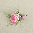 On a softly textured, light beige surface resembling fine linen or lightly woven burlap, a single pink rose boutonniere has been carefully laid out as if awaiting its place on a lapel in Mill Hill. The rose is angled slightly across the lower left of the scene, its petals layered in a tight rosette that fades from deep magenta edges into a tender, baby pink centre, giving the impression of a freshly opened flower at its most beautiful. Around it, clusters of pure white baby's breath create a delicate halo, each tiny bloom offering airy contrast and echoing the joyful mood of a wedding or prom near Mill Hill East or along The Ridgeway. Slender, grass-like sprigs of greenery emerge from behind the rose, stretching out with a sense of gentle movement, while a broader, deep green leaf curls protectively around the base, shaping itself into a natural, elegant collar. A scattering of water droplets rests on the leaf and petals, glistening faintly and suggesting the boutonniere has been recently misted to preserve its freshness for a special day. The stems beneath are meticulously bound with a smooth, pale pink satin ribbon, wrapped in precise, even turns, and finished at the base with a small, neatly tied bow in a deeper magenta-pink style that subtly echoes the richer tones of the rose. Against the understated background, every nuance stands out-the velvet of the petals, the fine froth of gypsophila, the sleek sheen of ribbon-creating a composed and romantic accessory, ideal for weddings, black-tie events, or school celebrations in Mill Hill where understated elegance is prized.