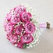 Beautifully arranged on a softly textured, light base evocative of Mill Hill's calm and welcoming charm, this classic round bouquet pairs tradition with creativity. At its core, a generous grouping of ten to twelve roses unfurls in a nuanced dance of colour-from silvery lavender at the innermost petals to bold, vibrant magenta tipping the outer layers. Interwoven throughout, fine white gypsophila adds frothy softness, giving the entire bouquet a dreamy, romantic presence similar to the early mist across Mill Hill's open fields. The stems are professionally gathered and finished with a lustrous pale pink ribbon, elegantly encircled by a spiral of lustrous white pearls that brings an artisanal touch and echoes the sophisticated atmosphere of local wedding venues. Exposed green-brown ends at the base underline the freshness and hand-tied craftsmanship. Gently illuminated by natural, diffused light, every petal's subtle shading and velvety texture are revealed, while the calm, neutral background allows the vivid blooms to shine. Perfect for marking engagements, weddings, or milestone anniversaries in Mill Hill, this arrangement tells a story of togetherness, artistry, and heartfelt joy, making it a treasured choice for celebrating love right here in the community.