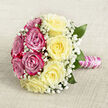 Placed on a subtly textured, neutral-toned cloth that resembles fine hessian or linen in soft beige, this hand-tied bouquet is photographed from a slightly elevated angle so its rounded form appears almost perfectly circular. The design is thoughtfully divided into two complementary halves: one side glows with rich fuchsia and magenta-pink roses, the other is bathed in the soft warmth of creamy yellow blossoms, each rose open to reveal its intricate swirl of velvety petals. Delicate sprigs of white baby's breath are tucked throughout the entire arrangement like tiny clouds, lending a light, airy quality that contrasts beautifully with the substantial rose heads. A few deep green leaves peek from beneath the blooms, adding structure and echoing the green views across Mill Hill's gardens and tree-lined streets. The stems are neatly arranged and bound in a classic hand-tied style, wrapped in smooth pink satin ribbon that catches a subtle sheen, then finished with a spiral of white pearls circling the handle, like a fine bracelet on a bride's wrist. The soft, diffused lighting allows the colours to appear gentle yet romantic, as if the bouquet were resting on a table in a Mill Hill bridal suite, moments before being lifted for a walk down the aisle. You can almost sense the fragrance: a blend of sweet rose, hints of freshness, and the quiet promise of celebration. This bouquet feels perfect for weddings, engagements, or milestone anniversaries in and around Mill Hill, a carefully crafted floral keepsake that mirrors the area's calm, elegant character.
