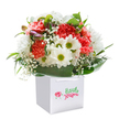Alive with joyful energy, this artful bouquet radiates the simple happiness of a sunny day in Mill Hill-fresh, generous, and expertly styled by neighbourhood florists. Coral and peach carnations form the main display, each flower's ruffled layers offering a lively sense of texture and natural beauty. Sprigs of snowy white daisies with yellow-lime centers nestle among the carnation blooms, their brightness lifting the arrangement with every glance, reminiscent of cheerful scenes along Hammers Lane. Light, feathery clouds of white baby's breath dot the bouquet, imparting an airy innocence and daydream-like charm. Framing the base, abundant, deep green foliage weaves a glossy, supportive structure around the flowers, bringing the ensemble to life and highlighting each individual stem. A few small, purple-tinged buds, still tightly closed, suggest a gentle surprise and a lovely sense of anticipation. Gathered within a clean white gift bag finished with sturdy ribbon handles, the bouquet stands ready to be shared-whether as a thoughtful gift for a birthday or a spontaneous gesture to add delight to someone's day in Mill Hill. The crisp white background amplifies the bouquet's colour and freshness, making this arrangement a reflection of care, optimism, and the timeless pleasure of receiving beautiful flowers from a trusted local florist.