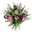 Against a crisp white background, a generous hand-tied bouquet glows with shades of pink, mauve, and fresh green, evoking the quiet elegance of a special delivery arriving at a doorstep in Mill Hill. At the centre, several pastel pink roses command attention, some tightly wrapped in bud form, others fully open so that their petal layers create delicate, spiralling rosettes. The colour gently shifts from a deeper blush in the centre to a softer, almost creamy edge, giving each bloom a sense of depth and softness. Embracing the roses are full, plush carnations in muted dusty rose and mauve, their generously frilled petals layering upon one another to form rich, textured cushions that feel both romantic and reassuring. Rising through this soft foundation, tall spikes of Veronica in deep violet-blue introduce height and sleek lines, lending a contemporary note to the otherwise classic look. Nestled among them, clusters of purple lisianthus provide velvety, bell-shaped blooms in a more saturated tone, offering pockets of rich colour that anchor the design. Scattered throughout are delicate, aster-like blossoms in light lavender-blue with tiny yellow centres, creating an airy, whimsical feel, like glimpses of wildflowers near Mill Hill's parks and gardens. The bouquet is wrapped in a collar of foliage: bright lime-green textural filler adds sparkle and energy, while cool, silvery eucalyptus leaves and soft green sprigs set a soothing backdrop. The stems at the base are neatly gathered and trimmed, clearly revealing the hand-tied style ready to be placed in a favourite vase. The overall impression is one of thoughtful refinement and gentle celebration, ideal for birthdays, anniversaries, or simply brightening a home across Mill Hill and neighbouring North West London areas.