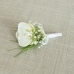 A single white orchid boutonniere rests on a softly textured, light beige fabric that looks like finely woven linen, its neutral tone reminiscent of the calm interiors of Mill Hill's quiet residential streets. At the heart of the design, a pristine Phalaenopsis orchid bloom opens with graceful, rounded petals, their surface velvety and gently glossy, catching the light in a subtle sheen. The orchid's throat reveals a delicate wash of pale yellow and a hint of cream, adding warmth and depth to the otherwise snowy white flower, like the first touch of sunrise over Mill Hill Park. Surrounding this central bloom, a halo of tiny white baby's breath blossoms creates a cloud-like frame; the Gypsophila is airy and light, each minute flower floating on slender green stems, softening the outline of the orchid and giving the boutonniere an ethereal, romantic quality. Fine, feathery greenery, similar to delicate maidenhair or asparagus fern, slips through the composition, its fresh, vibrant green tones bringing life and movement, as if a whisper of the hedgerows along Bittacy Hill has been tucked into the design. The stems are neatly gathered and expertly secured with a smooth white satin ribbon, wrapped tightly and finished with a small, understated bow that lies close to the base, clearly prepared to be pinned to a lapel. The lighting is gentle and even, without harsh shadows, allowing the crisp whites, soft creams, and bright greens to stand out clearly against the natural background. The overall mood is one of quiet sophistication and pure, understated elegance, perfectly suited to a Mill Hill wedding ceremony, a groom's jacket at Sacred Heart Church, or a prom corsage for a formal evening overlooking the green spaces of north London.