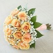This hand-tied bouquet, carefully crafted by florists in Mill Hill, exudes quiet elegance and heartfelt romance. A tight cluster of warm peach roses sits at the centre, each flower opening in a soft spiral and glowing from creamy blush through to sun-kissed apricot-a palette as gentle and uplifting as the dawn light on Watford Way. Sprigs of airy white gypsophila nestle between the roses, lending an effect not unlike fine lace or a bridal veil, their delicate appearance framing the bouquet with lightness. Glossy, deep green leaves provide a vibrant contrast and sense of renewal, reminiscent of strolls through the leafy spaces along Daws Lane. The stems are neatly wrapped with a wide ribbon in soft peach, carefully dotted with rows of pearlescent beads, offering a classic, tactile finish against the palm. Placed upon a neutral woven fabric, the entire design glows softly, infusing the composition with joy, hope, and the unique intimacy of a Mill Hill celebration-whether for a wedding, an anniversary, or another cherished milestone. Its gentle fragrance and harmonious palette create an atmosphere of tender anticipation, making this bouquet a true emblem of memorable moments in North London.