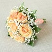This radiant bridal bouquet, presented diagonally across a pale, lightly textured linen backdrop, features a core of seven to nine lavishly bloomed roses in enchanting hues of peach, apricot, and soft coral. Each flower's petals unfurl gradually, displaying natural beauty and hinting at the abundant gardens found across Mill Hill. Wispy clouds of white baby's breath thread delicately through the bouquet, brightening the arrangement and enhancing the atmospheric sense of celebration. Discrete touches of dark green foliage emerge from among the blooms, adding lush depth and grounding the pastel tones. The classically rounded structure of the bouquet and the skillful gathering of the stems reflect expert composition and a careful personal touch. At the base, a coral-blush ribbon wraps the stems, its texture recalling both tradition and modern flair, while petite, white faux pearls spiral along the handle, suggesting vintage elegance-a fitting tribute to the classic tastes of Mill Hill. Subtle, even light magnifies the intricate details of every flower, leaf, and pearl, bringing the bouquet to vibrant life and making it ideal for weddings, bridal showers, or special events celebrated within the local community. Crafted for joyful occasions, this arrangement embodies romance, refinement, and the enduring artistry of Mill Hill's floral traditions.