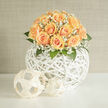 This hand-crafted composition marries soft peach roses with frothy clouds of white gypsophila, forming a rounded, tactile bouquet that feels both modern and timeless. Each rose unfurls in concentric spirals, a buttery dance of petals that shifts from pale cream to apricot, while the baby's breath threads through like silk, catching highlights and adding an ethereal hush. The flowers are arranged atop a sculptural white woven sphere - an openwork rattan orb whose criss-crossing lines create pockets of light and shadow, lifting the blooms with an airy, architectural grace. Green foliage peeks from beneath, grounding the palette and adding a faint green, resinous scent to the sweeter rose perfume.

The scene is softly lit, with warm daylight skimming each petal and giving the whole arrangement a faint golden halo. Perfect for a wedding, a milestone celebration, or as a refined centrepiece in a Mill Hill home, the bouquet evokes the quiet joy of new beginnings. I imagine it arriving by hand to a flat near Mill Hill Broadway or being chosen by a couple exchanging vows close to local parks - a design that reads beautifully in both contemporary apartments and village-style interiors. Prepared with the attentive eye of a local florist, this piece balances texture, tone, and form, and is ideal for customers seeking a graceful statement that feels personal and distinctly of the neighbourhood.