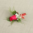 A single handcrafted boutonnière is laid gently on a soft, linen-like fabric in pale beige, the neutral background allowing every detail of the flowers to stand out clearly. At the centre sits a tightly furled fuchsia rosebud, its deep pink petals velvety and rich, holding the promise of full bloom. Nestled closely around the rose are tiny clusters of white baby's breath, like little clouds of foam, softening the bold colour and adding a light, romantic haze. Slender, bright green, feathery foliage - reminiscent of asparagus fern or fine ruscus - fans out from behind, giving the piece a sense of movement and airy elegance, as if caught in a gentle Mill Hill breeze drifting over from nearby Windsor Open Space. Broader, darker green leaves sit lower down, creating a stable base that frames the rose and filler flowers. The stems are neatly gathered and bound in a glossy red satin ribbon, wrapped with the precision of an experienced florist and finished in a tidy, compact band that catches the light with a subtle sheen. The overall composition feels calm yet celebratory, ideal for a groom's lapel or prom suit, with the warm, even lighting revealing the natural textures of petal, leaf, and fabric. This is the sort of refined, personal floral detail you might choose for an intimate wedding at a local Mill Hill venue, a quiet civil ceremony at the register office, or a special evening out, where a single rosebud speaks of romance, care, and understated style.