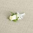 Placed gently on an oatmeal-hued linen fabric that could easily belong to a well-loved Mill Hill home, this wedding boutonnière radiates understated elegance. At the centre, a creamy ivory rose sits proudly, its petals smooth and velvety, curling inward with a graceful, natural symmetry that catches the light in soft highlights and shadows. Surrounding the rose, a collar of baby's breath-tiny white gypsophila blossoms-creates a cloud-like frame, their fine stems and star-shaped flowers bringing a sense of purity and tenderness. Threaded through this softness are fine strands of ornamental grass, bright green against the neutral background, giving the arrangement a gentle sense of movement and a fresh, garden-like character that feels at home near Mill Hill Park or along Lawrence Street. The stems of the flowers are tightly wrapped in pristine white satin ribbon, the fabric gleaming subtly, and ending in a carefully tied, delicate bow. The lighting is even and calm, revealing every subtle fold of the rose petals, each little floret of the baby's breath, and the woven texture beneath. You can almost feel the cool touch of the satin, the resilience of the stems within, and imagine the subtle, clean fragrance of the rose rising as it is pinned to a lapel for a wedding at a local church or venue near Mill Hill Broadway. This small, thoughtfully balanced boutonnière speaks of meaningful moments, expert local floristry, and the gentle joy of wearing a flower close to the heart.