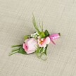 This gracefully composed boutonniere-ideal for weddings, proms, or memorable celebrations in Mill Hill-lies gently upon a pale, woven linen background that echoes the calm of local parkland mornings. Centred on the design is a blush-pink rose, tightly furled and carrying the delicate fragrance and look of new beginnings. Alongside the rose, a lightly frilled lisianthus or alstroemeria bloom in gentle peach and blush tones spreads its petals, revealing hints of soft yellow and darker detail at its core. Sprigs of snowy baby's breath and perky green mini mums complete the florals, providing a gentle contrast and uplifting freshness reminiscent of Mill Hill's leafy settings. A harmonious blend of slender green grasses, feathery fern tips, and deeper, broad leaves creates a shapely and enveloping backdrop, with one large leaf skillfully wound around the base. This natural bouquet is finished with a glossy fuchsia satin ribbon, expertly tied in a petite bow that draws the eye and suggests celebration. The gentle natural light brings out each colour and texture against the subtly coarse, neutral background. Lovingly crafted by experienced Mill Hill florists, this boutonniere combines natural sophistication and local flair-an effortless statement of romantic style for those special moments in North West London.