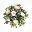 Top-down view of a hand-tied, circular bouquet resting against a pure white background, where the clean space around it makes every flower and leaf stand out clearly. At the heart of the design are creamy white roses, some fully open with spiralling, velvety petals, others still gently cupped, in soft shades of ivory and pale champagne. Threaded between them are deep purple and magenta Alstroemeria buds, their petals still mostly closed, with green-tinged bases that add a fresh, lively contrast. Fine sprays of white baby's breath weave through the roses and lilies like a soft mist, their tiny, cloud-like blooms giving the arrangement a light, airy feeling. A collar of dark green foliage frames the flowers, with broad, glossy leaves peeking between blossoms to create depth and a natural rhythm of light and shadow. The lighting is soft and even, rather like diffused daylight falling through a Mill Hill window, revealing the gentle sheen on each leaf and the fresh, plump texture of every petal. There is no visible vase, ribbon, or accessory; the focus is entirely on the flowers themselves, arranged with a calm, modern elegance. The bouquet feels romantic yet composed, suitable for a quiet anniversary at home off Mill Hill Broadway, a thoughtful sympathy gesture delivered near Mill Hill Park, or a simple thank-you that carries warmth without fuss. The overall mood is one of serene celebration and understated luxury, as if the bouquet has just been finished on the workbench of a local Mill Hill florist and set down for a final appreciative look from above.