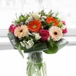 A visually striking bouquet crafted for Mill Hill displays a lively harmony of colour, form, and feeling. At the center, softly blushing peach gerbera daisies radiate gentle light, evoking the promise of a new day in local gardens or along Bittacy Hill. Pops of vibrant orange gerberas interject a burst of cheerfulness, reminiscent of the animated spirit of The Ridgeway. Deep magenta roses weave romance and richness through the ensemble, their velvety petals inviting pause and admiration. Interspersed ivory and white alstroemeria, alongside petite filler blossoms, breathe brightness and freshness into the design, much like the rejuvenating air that floats from Mill Hill's open spaces. The whole arrangement is framed by lush aspidistra leaves, broad and emerald, their curves both structured and inviting. Set in a tall, transparent glass vase that reveals the green stems, each element is showcased by a soft, radiant light akin to morning streaming through a window. Crafted thoughtfully by the local team, this bouquet brings joy, hope, and gratitude to every occasion-be it celebration, encouragement, or a simple gesture to brighten a Mill Hill home.