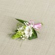 A delicately handcrafted boutonniere rests on a softly textured, light beige fabric that looks like natural linen, the neutral background allowing every petal and leaf to stand out with quiet clarity. At the heart of the piece is a single white alstroemeria bloom, its broad, gently ruffled petals opening wide to reveal fine reddish-brown speckles that gather towards the throat of the flower, and pale stamens that add a hint of depth at the centre. Tucked close beside it sits a lime-green conical cluster of tightly packed buds, similar to an Ornithogalum spike, its layered, scale-like texture bringing a sculptural, almost architectural feel to the small design. Around these focal elements, tiny white clouds of baby's breath float in and out, their miniature blossoms giving the impression of scattered snowflakes or a fine lace veil draped over the greenery. The foliage forms a confident frame, with dark green, sword-shaped leaves creating structure at the base, while slender, grass-like strands arc gently outward, adding movement and a sense of natural ease. At the right, the stems are gathered neatly and finished with a small, glossy pink satin ribbon tied into a tidy bow, the pop of colour adding a playful romantic note without overpowering the white and green palette. The light is soft and even, much like a calm Mill Hill morning, highlighting the freshness of the flowers as though they have just been prepared in a local studio, ready to be pinned to a lapel for a wedding, prom, or special celebration in one of the nearby parks or venues that dot this North London neighbourhood.
