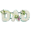 The photograph shows a personalised DAD funeral tribute, created with the kind of care and precision associated with local Mill Hill floristry. Three large, upright letters form the word, each one completely covered in tightly packed white chrysanthemums. The small, rounded blooms are arranged so closely that they create a continuous, cushion-like surface, with no stems or gaps visible. The petals, slightly ruffled and luminous against the white background, soften the strong shapes of the letters and evoke a sense of peace and purity. Around the edges of all three letters, a deep emerald green ribbon has been carefully pleated and fixed in place, tracing every curve and corner. This ruffled border frames the white flowers with a fresh, vibrant outline, reminiscent of the green landscapes surrounding Mill Hill. Subtle glimpses of a dark horizontal frame behind the flowers show how the letters are supported, holding them together as a single, freestanding tribute.
The arrangement is gently accented with tasteful floral sprays. On the upper left curve of the first D, a small posy of white freesia and glossy green foliage is nestled among the chrysanthemums, the freesia buds and delicate bells introducing texture and a hint of fragrance. Two long, slender green stems then arc diagonally across towards the central A, guiding the eye and linking the letters visually. At the lower right side of the A, where the stems meet, a more dramatic focal point emerges: two deep purple calla lilies, velvety and elegantly rolled, sit among more white freesia and bright greenery. Their rich colour brings depth and formality to the tribute without overpowering the calm, white base. The final D is adorned on its upper right edge with another, slightly smaller cluster of white freesia and foliage, echoing the first letter and completing the design.
Presented against a simple white background, the tribute feels quietly dignified and deeply personal. It is easy to imagine it being delivered by Flowers Mill Hill to a local church or crematorium, where it would stand as a clear, floral expression of love and remembrance for a father who will not be forgotten.
