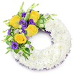 A tender, circular sympathy wreath shaped like a perfect 'O', crafted from hundreds of small, pristine white spray chrysanthemums that form a dense, cloud-like band of petals. The surface reads soft and tactile, each tiny bloom pressed close to its neighbour to produce a smooth, reverent texture that catches soft daylight and suggests quiet peace. Nestled into the upper left curve is a hand-tied spray of colour: several fully opened yellow roses with warm, buttery centers, their petals spiralling gently outward; alongside them, deep royal purple lisianthus (Eustoma) with ruffled, cup-shaped blooms and a few pale lavender-green buds waiting to unfurl. Shiny, rounded leaves and slender fern fronds weave between the flowers, some leaves showing a subtle variegation, giving the spray depth, movement, and a cool green contrast against the white. A fine dark-violet mesh ribbon peeks from beneath the chrysanthemum ring along the inner and outer edges, an understated trim that echoes the purple lisianthus and lends continuity to the composition. The overall palette-pure white, sunny yellow and velvety purple-feels simultaneously respectful and consoling, a visual language of remembrance that refrains from excess. As a Mill Hill florist would arrange for a local funeral or graveside service near Mill Hill Cemetery or a quiet memorial in Mill Hill Park, the design is made to convey tenderness and clarity: simplicity in form, richness in feeling, and a composed elegance that gently holds memory without overwhelming it. The image sits against a clean white background so the wreath's textures, colours and the fine craftsmanship of each placement read clearly to the eye.