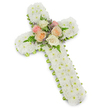 A peaceful floral cross, designed as a funeral or memorial tribute, appears against a stark white background, the gentle shadow beneath it revealing its three-dimensional construction. The cross is entirely cloaked in tight clusters of white button chrysanthemums, each tiny flower head placed so closely that they merge into a single, soft, snowy surface. This continuous white layer radiates a sense of purity and tranquillity, evoking quiet prayer and reflection. Around the very outer edge, a narrow lime green ribbon is wrapped with care, forming a slim border that subtly outlines the shape. Its fresh, spring-green tone offers a delicate contrast, reminiscent of the foliage and trees around Mill Hill's quiet residential streets and churchyards. At the very centre of the cross, where its arms meet the vertical stem, the texture shifts from small chrysanthemums to a compact spray of larger blooms. Fully opened roses in soft pastel shades-pale pink, creamy white, and warm peach-are nestled together, their velvety petals unfurling in layered spirals. Sprigs of airy green fern and tiny lavender-tinted filler flowers weave between the roses, introducing gentle depth, movement, and a hint of colour that doesn't overwhelm the overall serenity. The composition feels balanced and intentional, with every flower working together to express love, respect, and faith. Crafted as a fitting tribute for services held in Mill Hill churches, crematoria, or local cemeteries, this floral cross stands as a symbolic gesture of condolence, offering visual comfort and a quiet message of hope and eternal rest to those gathered to say goodbye.