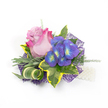 A delicate handcrafted corsage or boutonniere photographed on a crisp white background, composed around a single partially open rose whose petals melt from a soft lavender-pink at the heart into a vivid fuchsia at the outer edges. Beside it, a compact spray of indigo-purple florets-suggestive of hydrangea-catches the eye with tiny bright blue and yellow-green centers that glow like garden jewels. The blooms sit within a textured frame of foliage: broad variegated ivy leaves with deep emerald centers and sunny lemon-yellow margins, narrow silvery-green leaves that suggest lavender foliage, and fine, airy sprigs reminiscent of asparagus fern that lend a whisper of movement. A sculptural curled blade, striped in green and cream, adds a contemporary twist and an elegant line to the shape. Underpinning the composition is an intricate, web-like layer of dark purple mesh that peeks out to provide depth and modern contrast, while a short strand of lustrous white pearls at the lower right hints at a wristlet or a refined fastening. The studio lighting is soft and even, bringing out the velvety texture of the rose and the subtle sheen of the pearls without harsh shadows; you can almost sense the rose's faint heady perfume and the cool, crisp feel of the greenery. Designed with celebrations in mind-weddings, proms, or graduations-this compact accessory balances romance and contemporary flair. As a florist familiar with Mill Hill's quieter lanes and community events, I imagine this pinned to a lapel on The Ridgeway or worn for photos in Mill Hill Park, where its colours would read vividly against spring or evening light.
